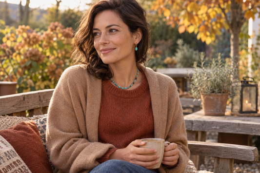 Vrouw met turquoise oorbellen en een kralenketting, een roestkleurige trui en camel vest op een gezellig herfstterras.